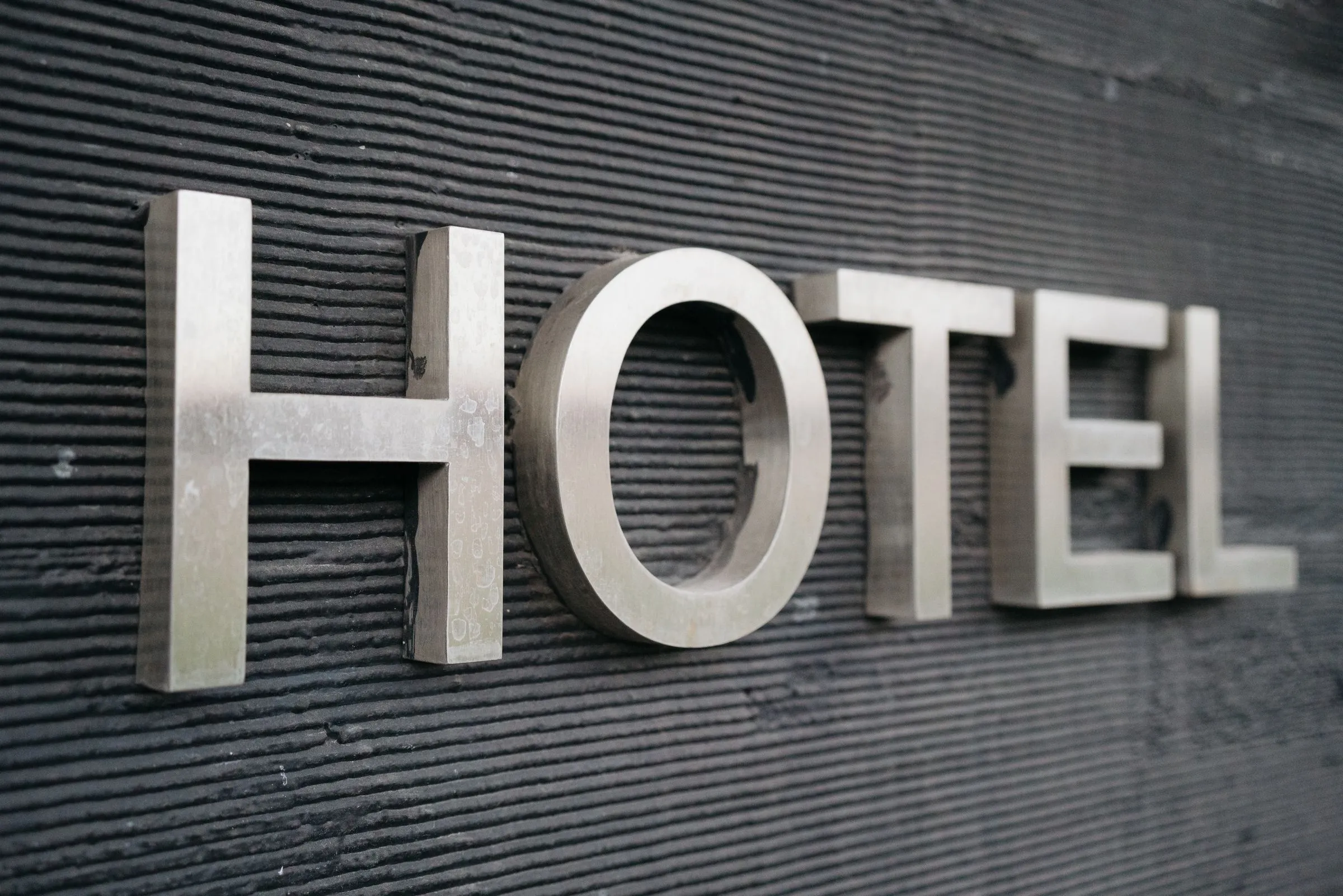 Edelstahlbuchstaben „Hotel“ an einer dunklen, gerillten Fassade